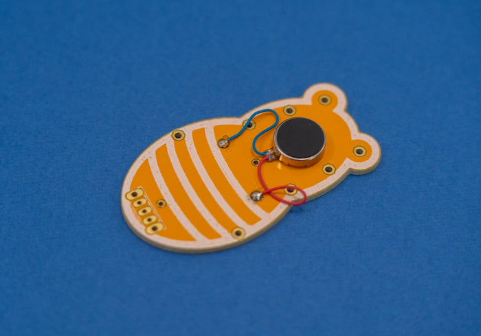 Bee-shaped yellow and white PCB with a black motor and red and blue wires on a solid blue surface.