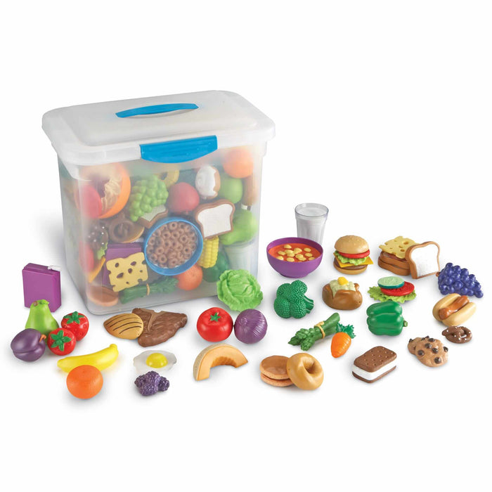 Colorful plastic toy food pieces like fruits, veggies, and snacks spread out next to a clear plastic storage bin.