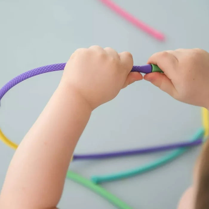 Child’s hands connect a purple textured rod to a green tip. Other colorful rods lie on a light gray surface.