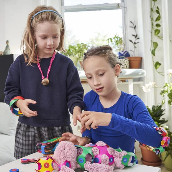 Two kids play with vibrant, flexible magnetic building pieces to decorate a stuffed bunny and wear as creative jewelry.