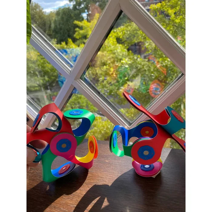 Two vibrant, flexible 3D structures made of colorful magnetic building pieces on a sunlit wooden surface.
