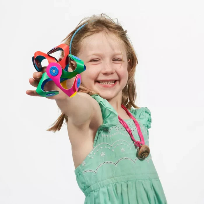 Smiling girl holds a colorful 3D star built from flexible magnetic pieces in red, green, blue, and pink.