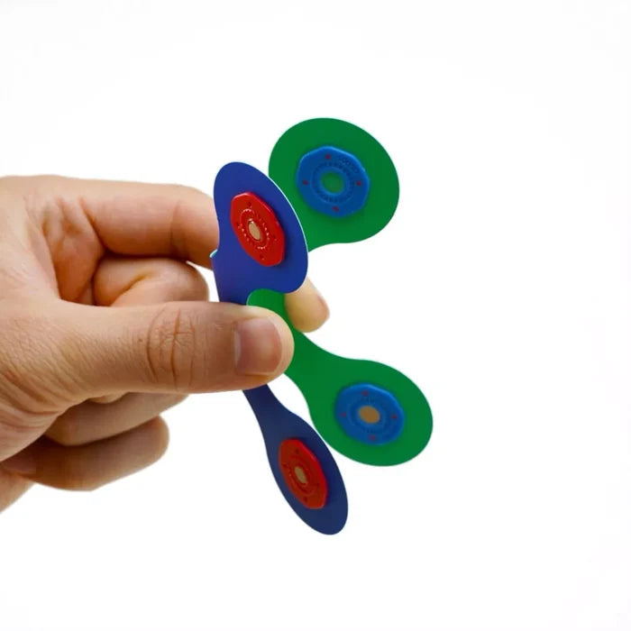 Hand holding flexible blue and green magnetic toy pieces with round red and blue snap connectors.