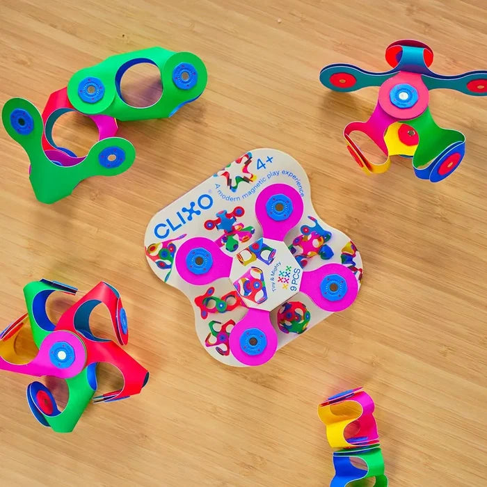 Colorful flexible magnetic building pieces and 3D shapes surrounding a white package on a light wood surface.
