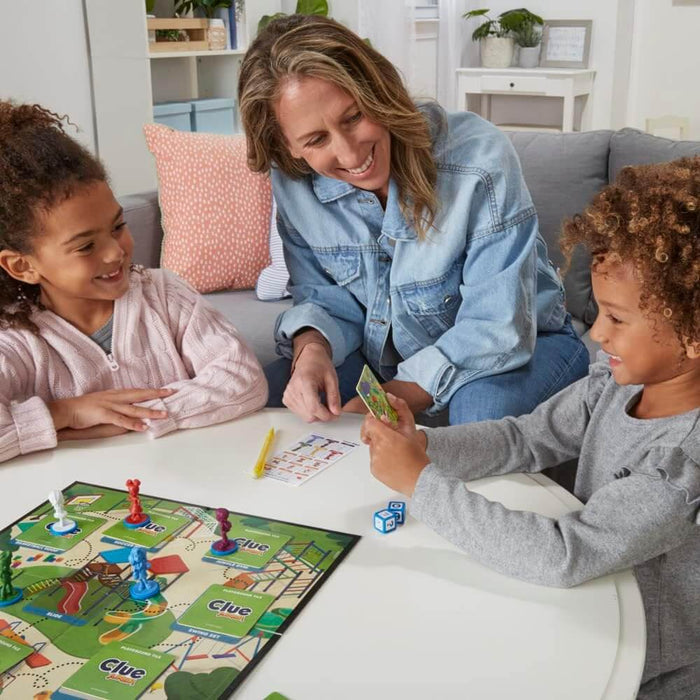 Woman and two children play a board game with colorful figurines, blue dice, and a playground map on a white table.