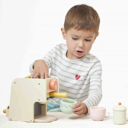 Child playing with a cream wooden toy espresso maker with colorful dials and pastel cups.