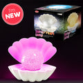 White shell lamp with a glowing pink glitter pearl inside, shown with its product box and a red I'm NEW sticker.