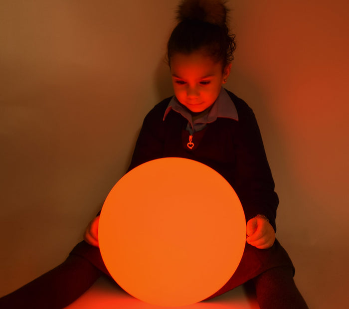 A child sitting behind a large, glowing orange sphere that illuminates their face and surroundings.