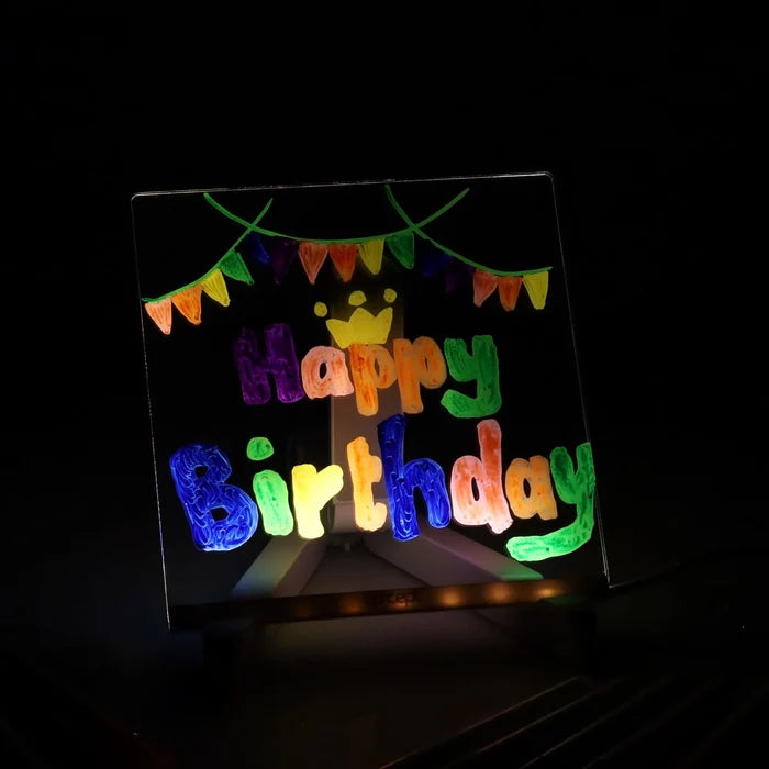 Square LED board glowing in the dark with colorful hand-drawn Happy Birthday text, crown, and festive bunting.