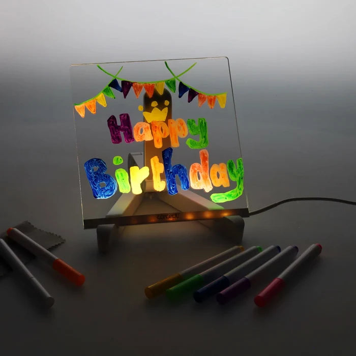 Square acrylic LED board with a glowing colorful Happy Birthday message, wooden stand, and assorted markers.