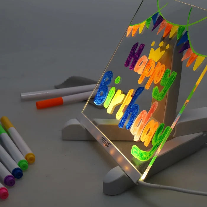 LED-lit square acrylic board on a stand with a glowing neon Happy Birthday message and colorful markers nearby.