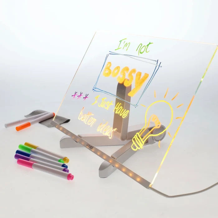 Clear LED acrylic board on a stand with neon handwritten text, a lightbulb drawing, and several colorful markers.