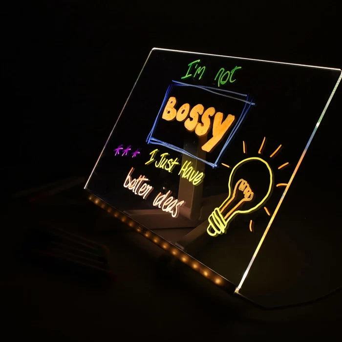 Acrylic LED board glowing with colorful text I'm not BOSSY and a hand-drawn yellow lightbulb in the dark.