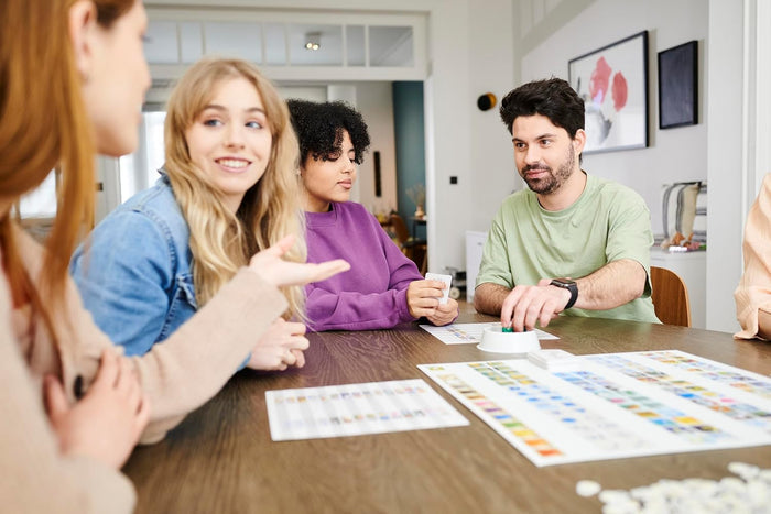 Four friends playing Concept board game featuring a white board with colored icons and green game pieces.