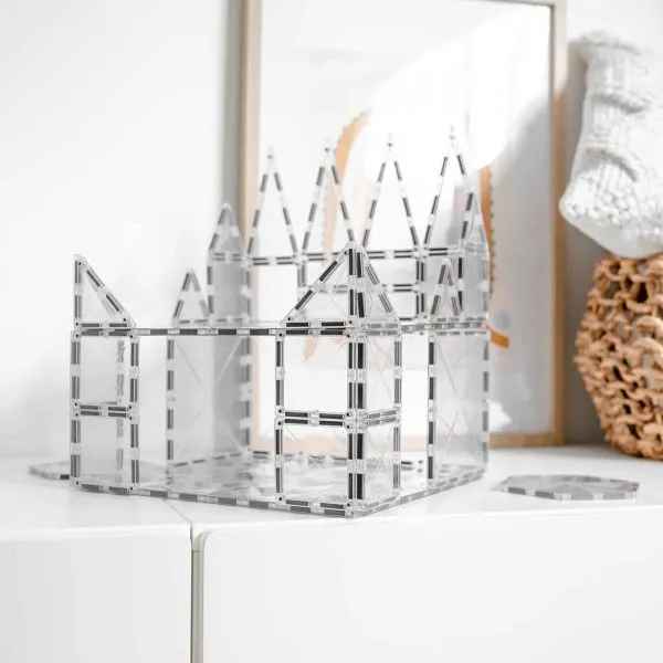 Clear magnetic building tiles shaped into a castle with pointed towers on a white shelf.