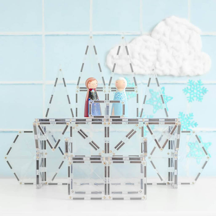 A toy ice palace built with clear square and triangular magnetic tiles, featuring two small wooden dolls.