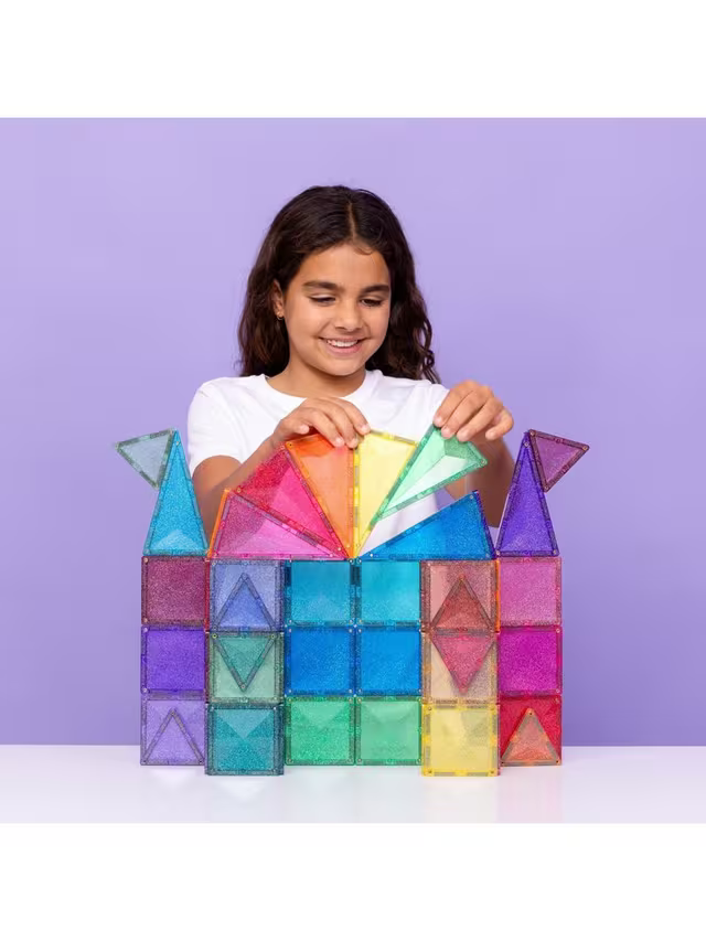 A girl building a rainbow castle structure with glittery, translucent magnetic squares and triangles.