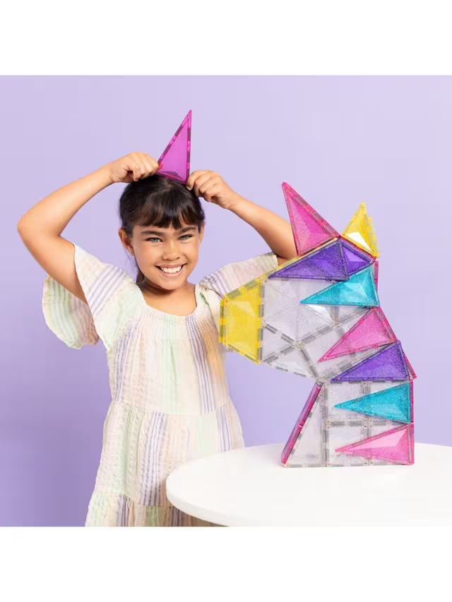 Girl with a purple tile horn next to a colorful unicorn head built from glittery, translucent magnetic tiles.
