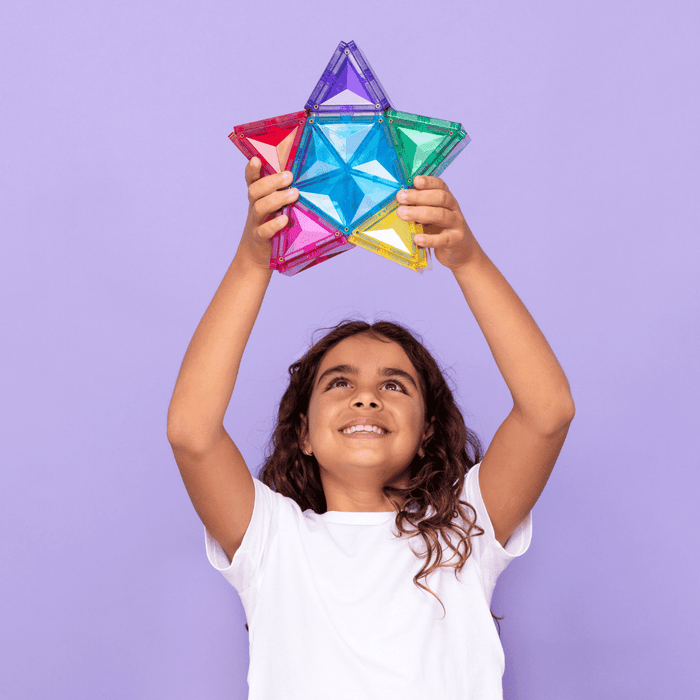 A child holds a large star made of colorful, translucent magnetic tiles against a solid purple background.