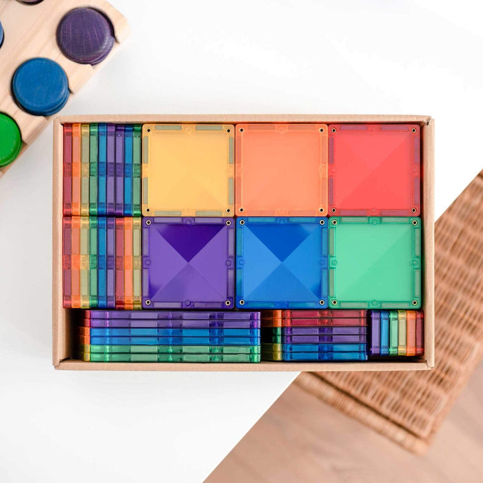 Rainbow-colored translucent square magnetic tiles neatly stacked and organized in a cardboard box.