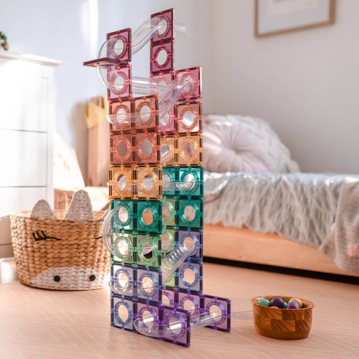 Tall ball run tower built with pastel magnetic tiles and clear plastic tubes in a child's bedroom.