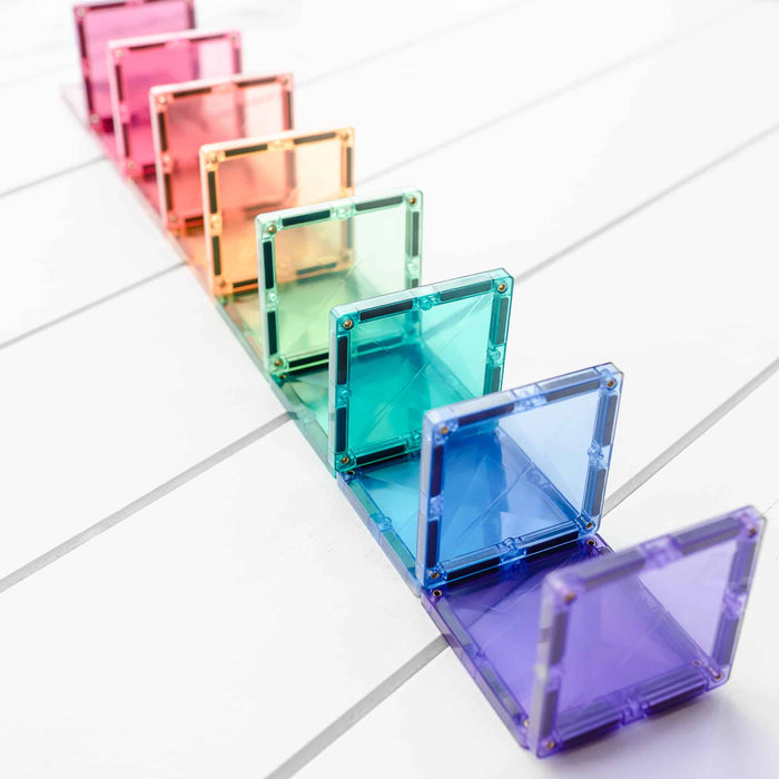 Translucent pastel rainbow square magnetic tiles standing in a row on a white wooden tabletop.