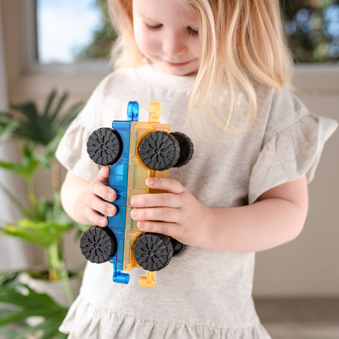 Child holding one blue and one yellow translucent magnetic toy car base with black wheels.