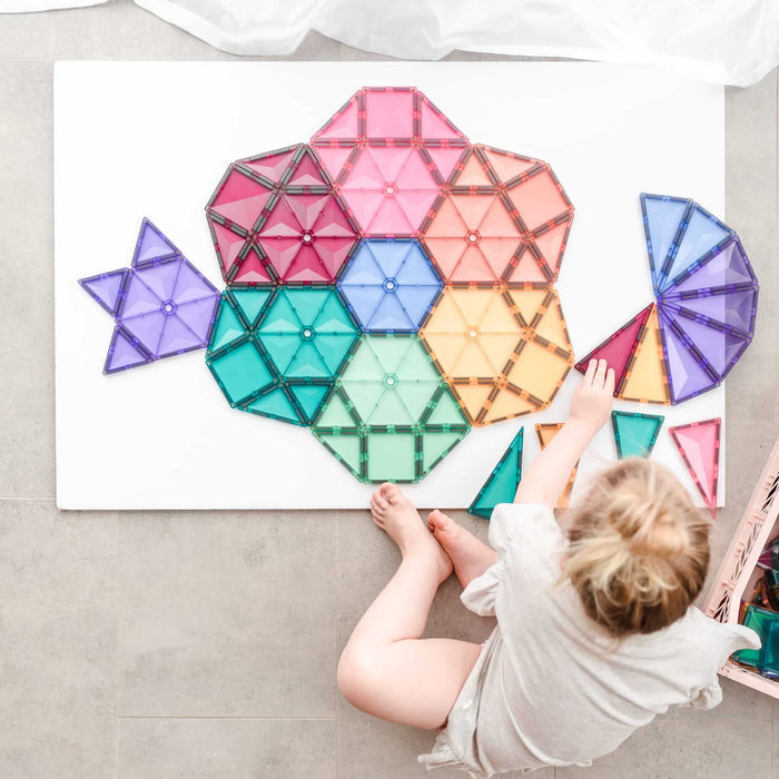 Child arranging pastel-colored magnetic triangles and hexagons into a large geometric pattern on a white surface.