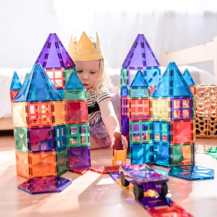 Child builds tall castles using vibrant, translucent magnetic tiles in rainbow colors and geometric shapes.