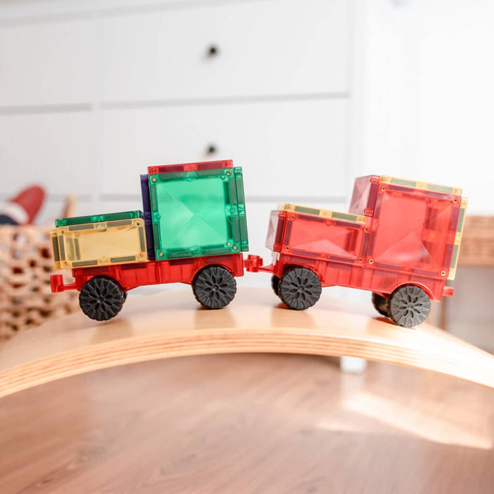 Colorful magnetic tiles built into a toy truck and trailer with wheels on a curved wooden board.