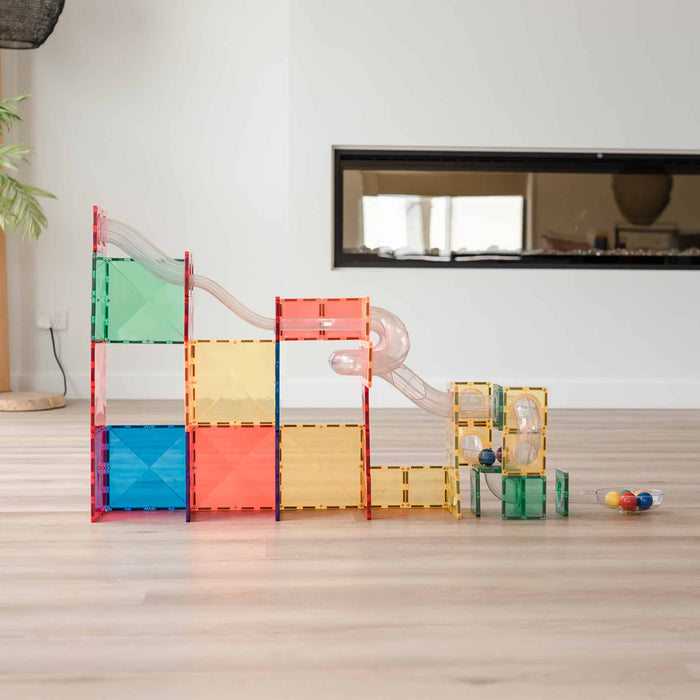 Colorful magnetic tile ball run with translucent squares, clear tracks, and small balls on a light wooden floor.
