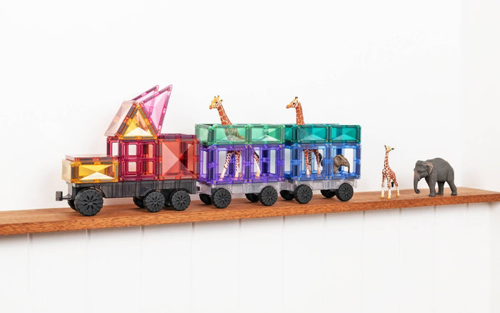 A toy truck and trailers built from pastel magnetic tiles carrying toy animals on a wooden shelf.