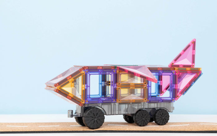 Toy vehicle built with pastel pink, purple, and orange magnetic tiles, wheels, and a tail fin on a toy road.
