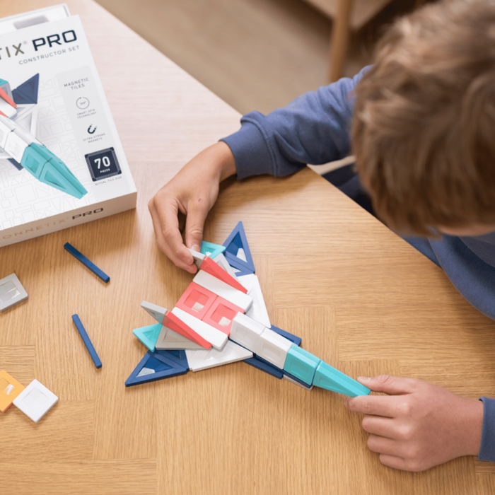 Child building a toy jet with colorful magnetic tiles on a wooden table next to the Connetix PRO set box.
