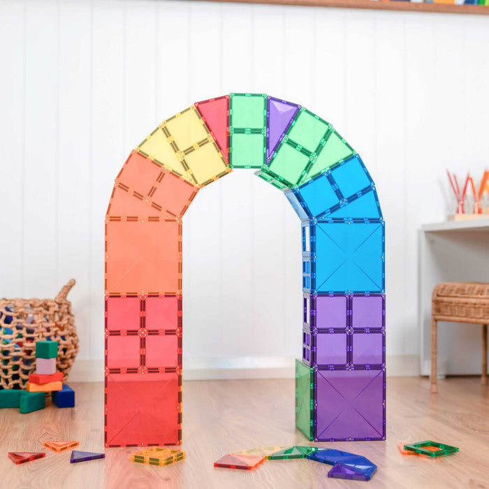A large rainbow arch built from translucent magnetic square and triangle tiles on a light wood floor.