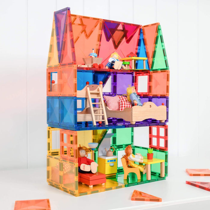 Tall dollhouse built with rainbow magnetic tiles, featuring wooden furniture and dolls inside on a white surface.