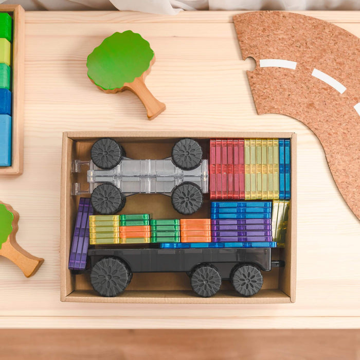 Translucent rainbow magnetic tiles and two toy vehicle bases neatly packed in a cardboard storage box.