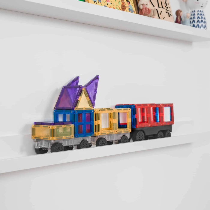 Magnetic toy train with translucent purple, blue, yellow, and red tiles on rolling wheel bases on a white shelf.