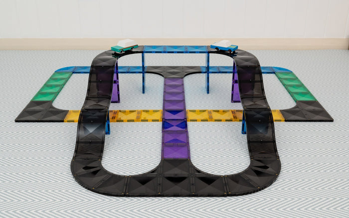 Toy magnetic tile set built into a multi-level track with black ramps, colorful paths, and two cars on a bridge.