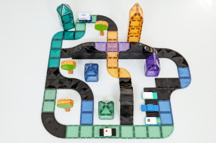 Vibrant magnetic tile road layout with black ramps, intersections, toy cars, and buildings on a white patterned surface.