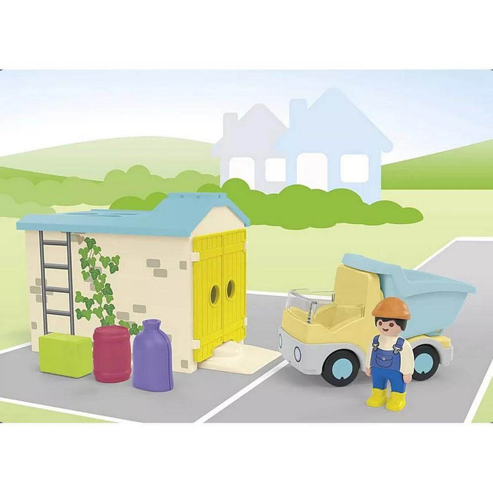 Playmobil Junior set with yellow dump truck, worker figure, and cream garage with blue roof and ladder.