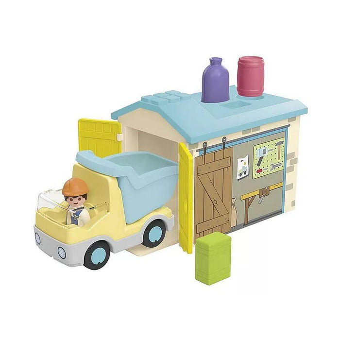 Yellow toy construction truck with driver figure and blue tipping bin inside a small garage with colorful accessories.
