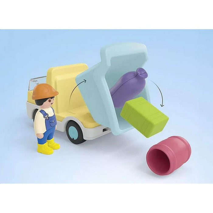Yellow toy truck with blue bin dumping a purple sack, green block, and red barrel next to a worker figure.