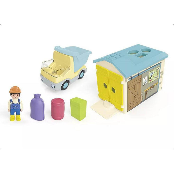 Yellow dump truck, blue-roofed shape-sorter garage, worker figure, and colorful toy accessories.