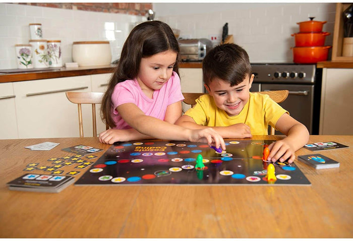 Two children play a space-themed board game with colorful rocket ship tokens and cards on a wooden table.