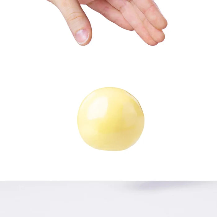 A hand reaches for a smooth, pale yellow ball of putty floating against a white background.