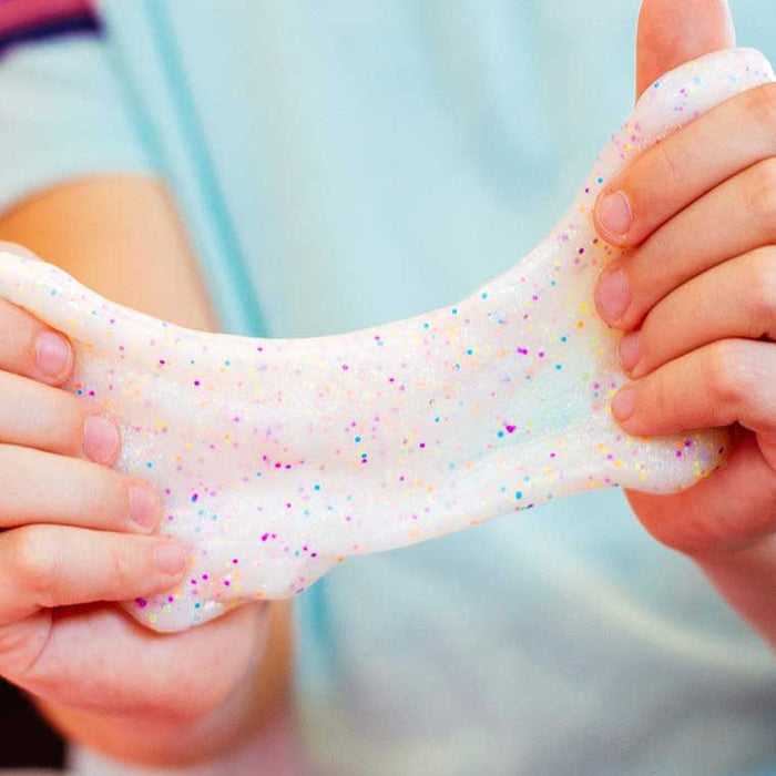 Hands stretching translucent white putty filled with multi-colored rainbow glitter and confetti.