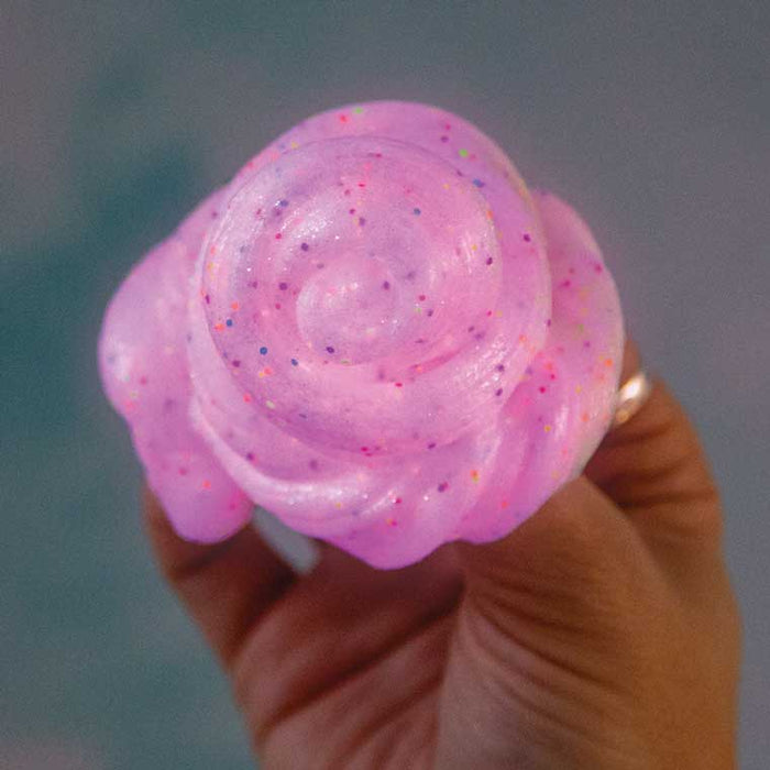 Hand holding a swirl of translucent pink putty filled with tiny multi-colored glitter specks.