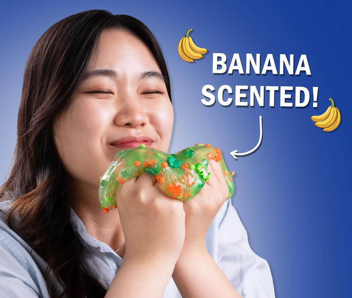 Smiling person smells translucent green slime with dinosaur charms; text says BANANA SCENTED! with banana icons.