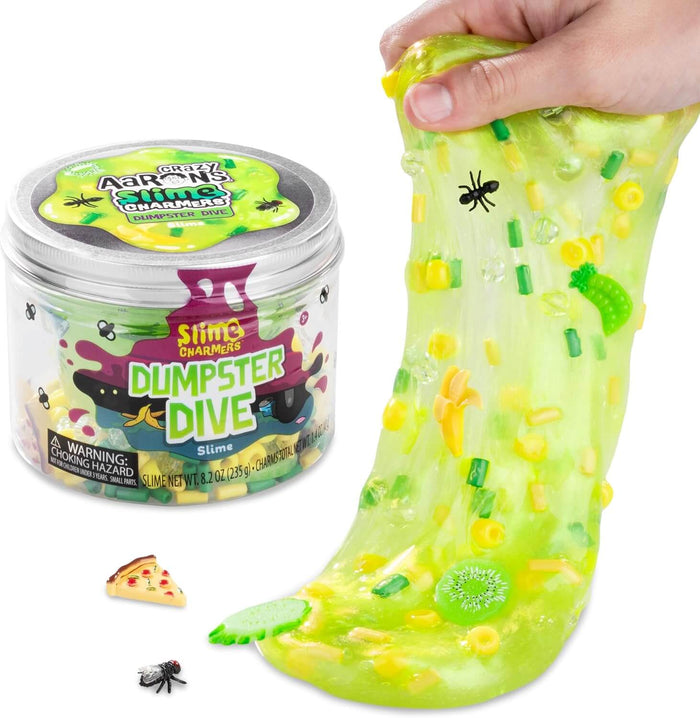 Hand stretching translucent neon green slime with fly, pizza, and fruit charms from its Dumpster Dive container.